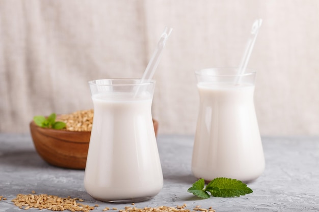 Biologische niet-zuivel havermelk in glas en houten plaat met haverzaden op een grijze betonnen ondergrond. veganistisch gezond voedselconcept, close-up, zijaanzicht.