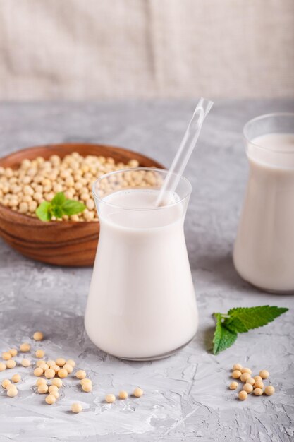 Biologische niet-zuivel sojamelk in glas en houten plaat met sojabonen op een grijze betonnen ondergrond. veganistisch gezond voedselconcept, close-up, zijaanzicht.