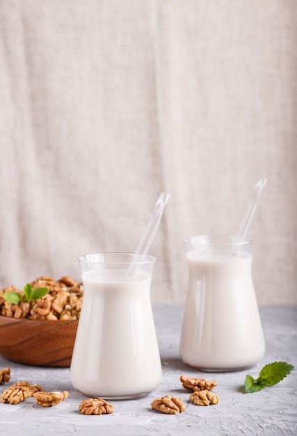 Biologische niet-zuivel walnoot melk in glas en houten plaat met walnoten op een grijze betonnen achtergrond.