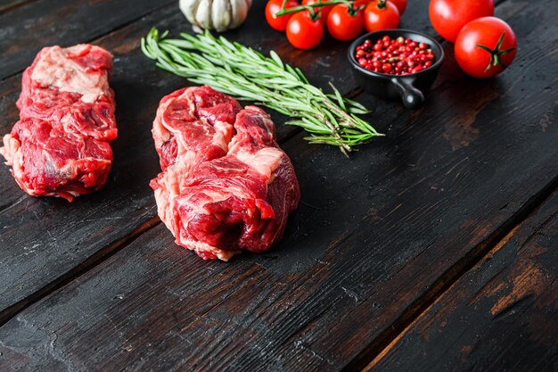 Biologische rauwe chuck eye roll biefstuk gesneden met rozemarijn rode onin knoflook peperkorrels en tomaten op oude donkere houten tafel Zijaanzicht met ruimte voor tekst