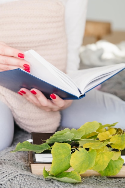 生物学者の趣味本と植物学を勉強している黄色の葉と一緒にベッドに座っている女性科学者のトリミングされたショット