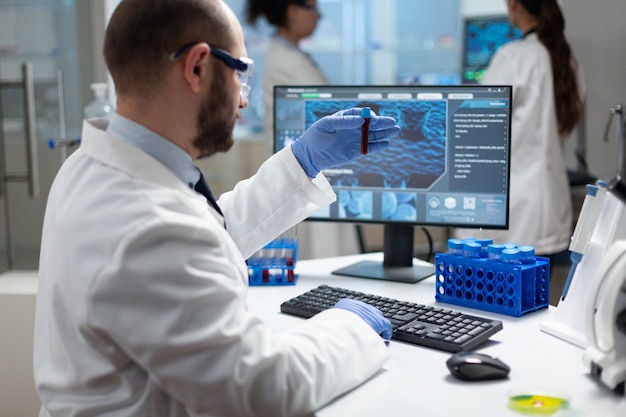 Photo biologist researcher man holding blood vacutainer analyzing dna sample working in microbiology hospital laboratory. scientist developing sickness treatment using modern biotechnology