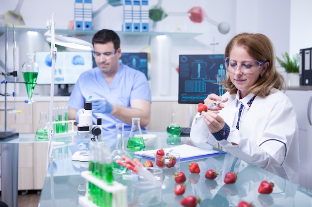 Biologist woman studying strawberries in a research lab. Scientist man working in the background.