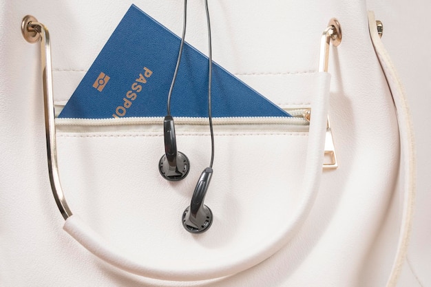 Biometric passport and headphones on it in a white female handbag, close-up