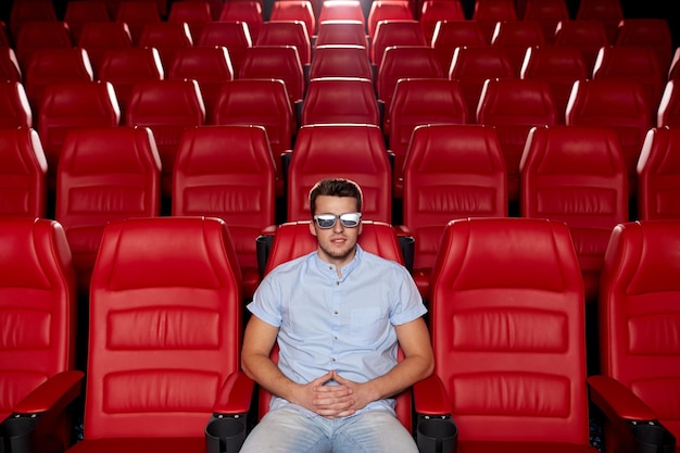 bioscoop, technologie, entertainment en mensenconcept - gelukkige jonge man met 3D-bril die alleen naar film kijkt in een leeg theaterauditorium