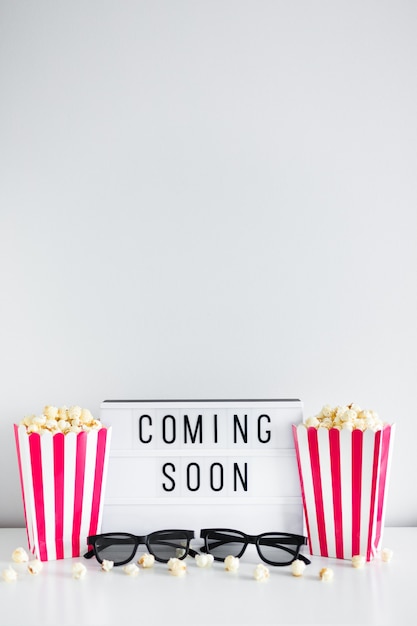 Bioscoopconcept - gestreepte dozen met popcorn, 3D-bril, lichtbak met "coming soon"-tekst en kopieerruimte op witte achtergrond