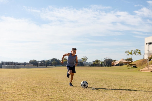 Biracial basisschool jongen voetballen op school voetbalveld tegen hemel tijdens zonnige dag