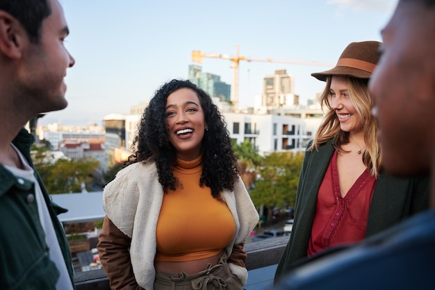 biracial female chatting to group of multicultural friends socializing on a rooftop terrace at dusk