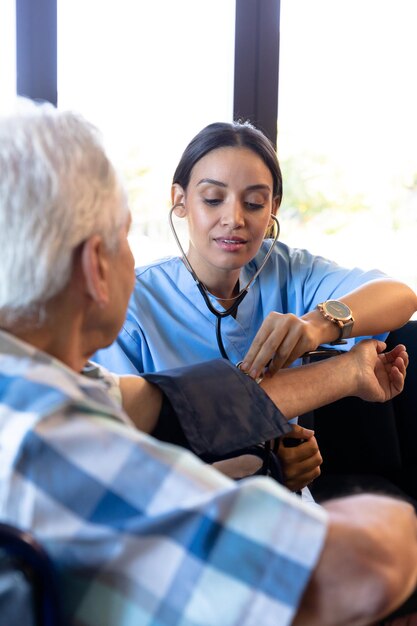 Biracial female doctor examining caucasian senior man's blood pressure with gauge and stethoscope