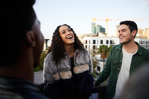 biracial female laughing with group of multicultural friends socializing on a rooftop terrace at dusk