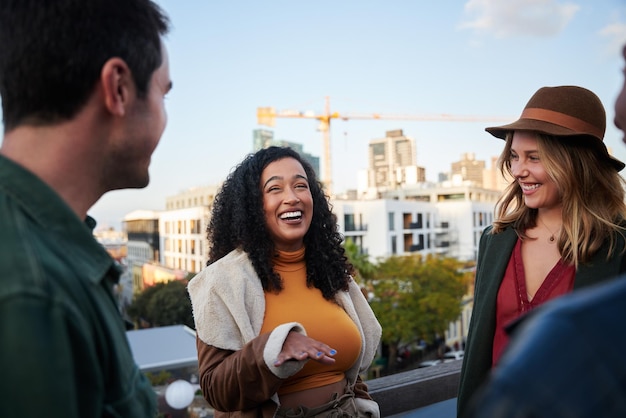 biracial female laughing with group of multicultural friends socializing on a rooftop terrace at dusk