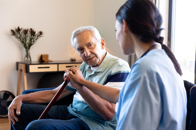 Photo biracial female physiotherapist consoling caucasian senior man sitting with walking cane on sofa