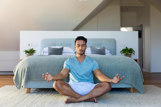 biracial man sitting on floor in bedroom, meditating