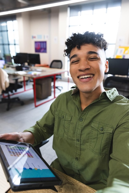 Biracial man smiling looking at the camera on smartphone during a video call at office. Business, technology and office concept