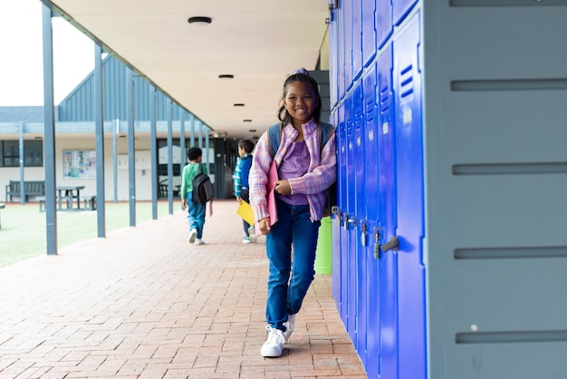 Biracial meisje met een heldere glimlach staat bij blauwe school lockers met kopieerruimte