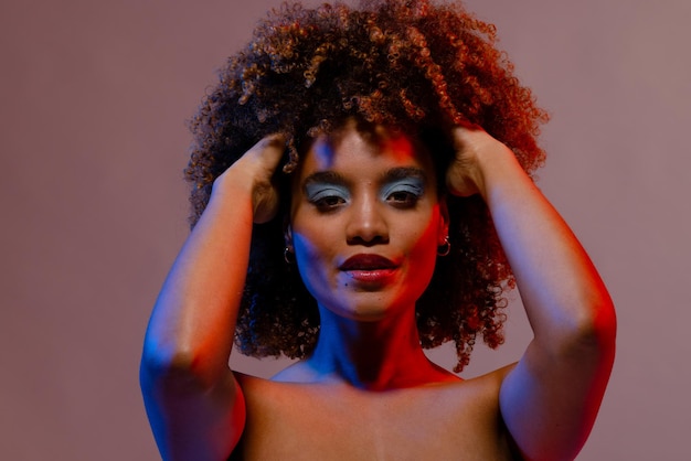Biracial woman in blue eye shadow with hands in curly hair in blue and red light