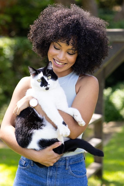 Biracial young woman holding black and white cat both outdoors at home in garden