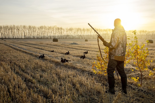 Bird hunting in autumn season at sunrise Hunter in camouflage with a gun hunting on birds