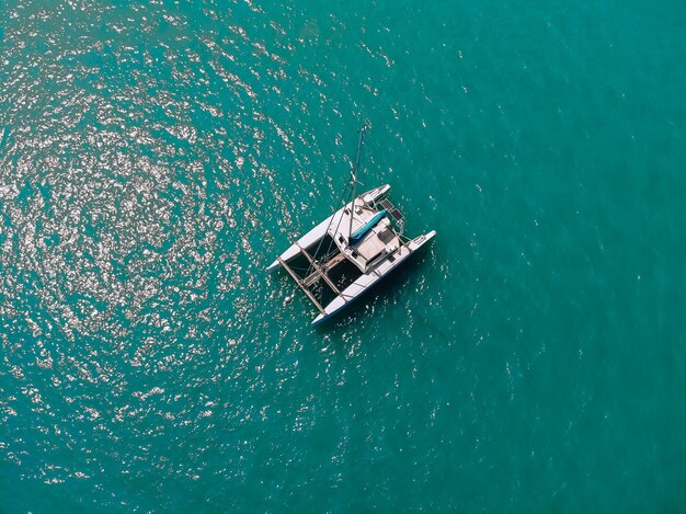 Bird's eyes view of the amazing white catamaran sailing across the blue lagoona. Top view.