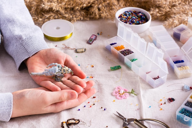 Photo bird woven from beads in children's hands among boxes with beads