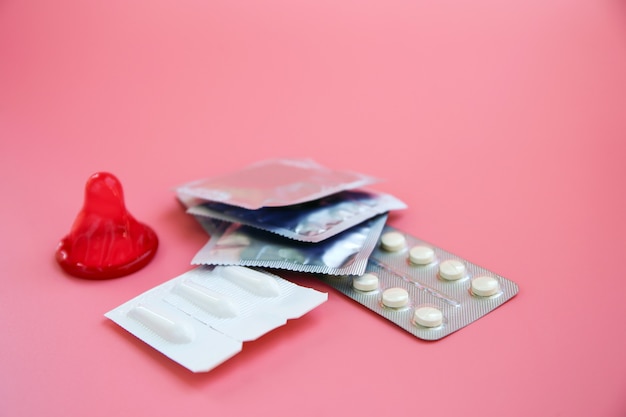 Birth control pill, vaginal candles, and condom on a pink background.