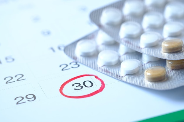 birth control pills and calendar on wooden surface, close up