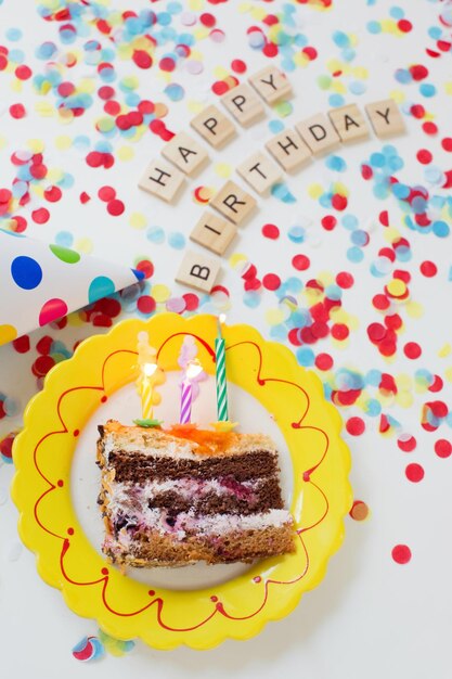 Birthday background with tasty cake on a plate paper party hat\
colorful confetti and wooden sign letters