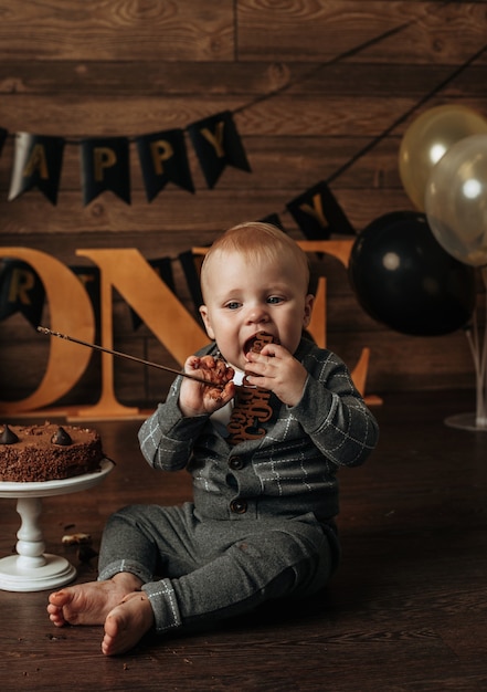 A birthday boy in a gray suit eats a chocolate cake on a brown background