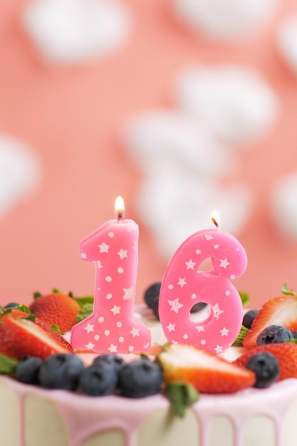 Birthday cake number 16 Beautiful pink candle in cake on pink background with white clouds Closeup and vertical view