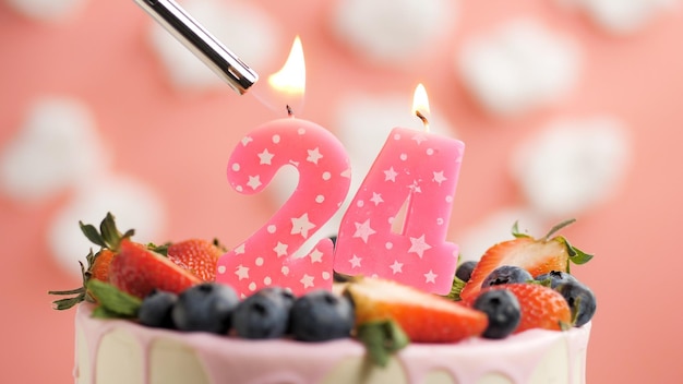 Torta di compleanno numero 24 candela rosa sulla bella torta con frutti di bosco e accendino con fuoco sullo sfondo di nuvole bianche e cielo rosa vista ingrandita