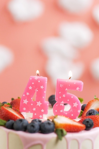 Birthday cake number 45 beautiful pink candle in cake on pink\
background with white clouds closeup and vertical view