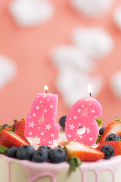 Birthday cake number 46 beautiful pink candle in cake on pink\
background with white clouds closeup and vertical view