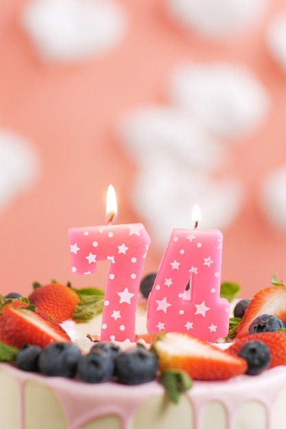 생일 케이크 번호 74 흰 구름이 있는 분홍색 배경에 케이크에 있는 아름다운 분홍색 촛불 근접 촬영 및 수직 보기