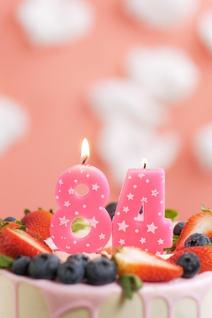 Birthday cake number 84 beautiful pink candle in cake on pink\
background with white clouds closeup and vertical view