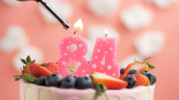 Foto torta di compleanno numero 84 candela rosa sulla bella torta con frutti di bosco e accendino con fuoco sullo sfondo di nuvole bianche e cielo rosa vista ingrandita