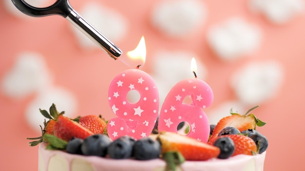 Birthday cake number 96 pink candle on beautiful cake with berries and lighter with fire against background of white clouds and pink sky Closeup view