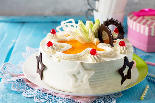 Birthday cake sponge cake with whipped cream with colorful candles on a blue background