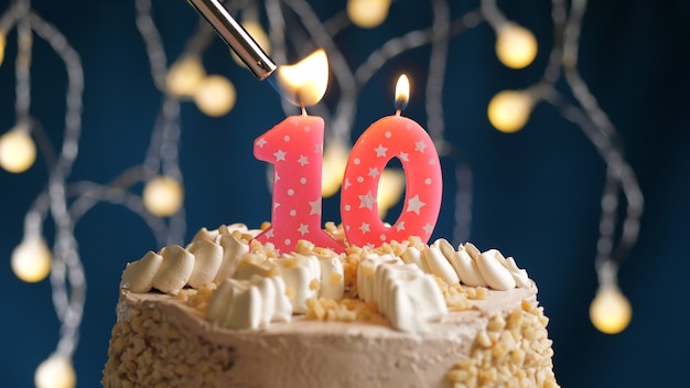 Foto torta di compleanno con una candela rosa a 10 numeri su sfondo blu incendiata da un accendino. vista ravvicinata