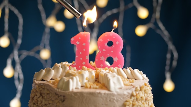 Birthday cake with 18 number pink candle on blue backgraund set on fire by lighter. Close-up view