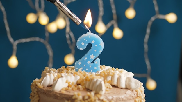 Photo birthday cake with 2 number candle on blue backgraund set on fire by lighter. close-up