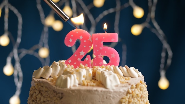 Birthday cake with 25 number pink candle on blue backgraund set on fire by lighter. Close-up view