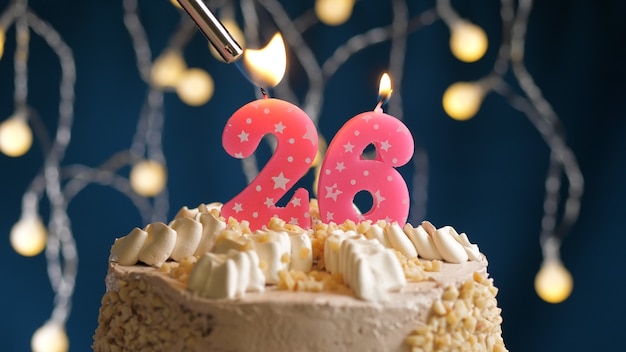 Photo birthday cake with 26 number pink candle on blue backgraund set on fire by lighter. close-up view