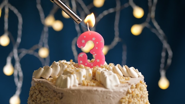 Birthday cake with 3 number pinkcandle on blue backgraund set on fire by lighter. Close-up view