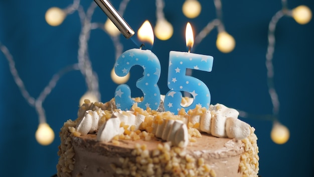 Photo birthday cake with 35 number candle on blue backgraund set on fire by lighter. close-up