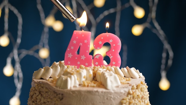 Photo birthday cake with 43 number pink candle on blue backgraund set on fire by lighter. close-up view