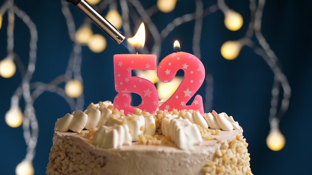 Photo birthday cake with 52 number pink candle on blue backgraund set on fire by lighter. close-up view