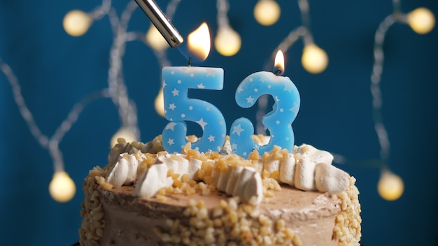 Birthday cake with 53 number candle on blue backgraund set on fire by lighter. Close-up