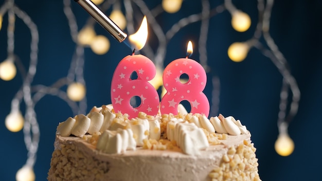 Торт ко дню рождения с розовой свечой номер 68 на синем backgraund, подожженный зажигалкой. Вид крупным планом