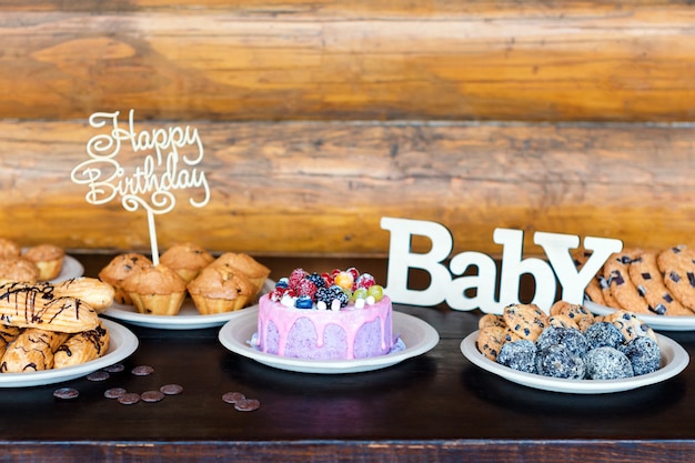 Birthday cakes and muffins with wooden greeting signs on rustic wall. Wooden sing with letters Happy Birthday, Baby and holiday sweets.