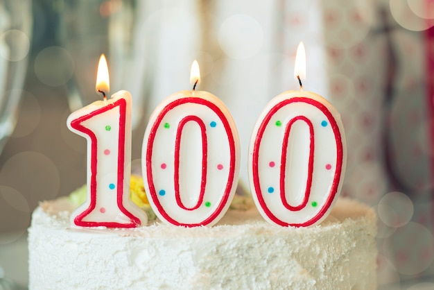 Photo birthday candle as number one hundred on top of sweet cake on the table, 100th birthday